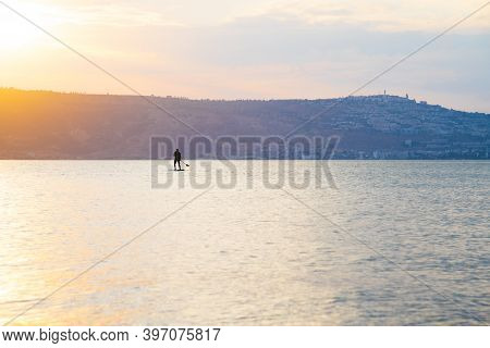 Man Sail On A Sup Board In A Large Lake During Sunrise. Stand Up Paddle Boarding - Active Recreation