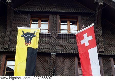 Banners Of The Canton Uri And Switzerland Hanging In Front Of A Typical Wooden Chalet In Andermatt, 