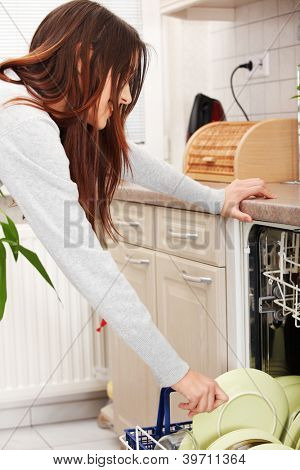 Giovane donna in cucina rassettando. Tirando fuori piatti dalla lavastoviglie