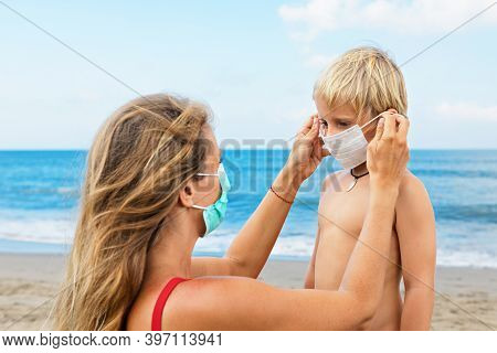 Mother Put Medical Mask On Child On Sea Beach. New Rules To Wear Cloth Face Covering At Public Place