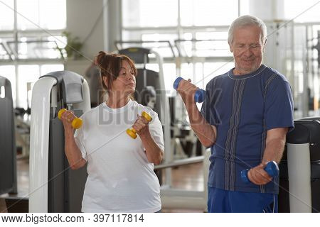Seniors Lifting Weights At Gym. Elderly Couple Lifting Dumbbells At Fitness Center. Weight Training 