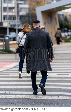 Handsome Man On Street Background. Crossing The Street Back To The Camera. Dark Gray Coat On.