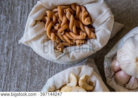 Variety Of Different Groceries In Cotton Bags Packed For Storage: Pasta, Nuts, Garic On Stone Backgr