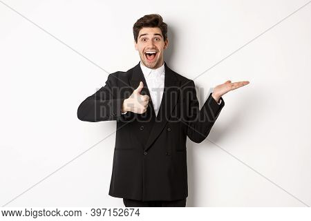 Portrait Of Hadnsome Bearded Man In Formal Suit, Showing Thumb-up And Holding Product In Hand Over W