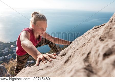 Purposeful Young Girl Climbs To Top Of Mountain. Courage And Concentration. Fingers Clinging To Rock