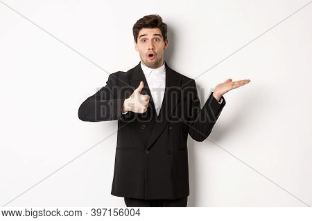 Portrait Of Hadnsome Bearded Man In Formal Suit, Showing Thumb-up And Holding Product In Hand Over W