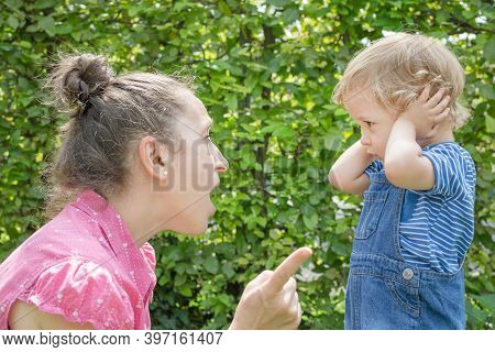 Angry Mother Shout At Her Naughty Son In The Park While The Little Child Cover His Ears Avoiding Mad