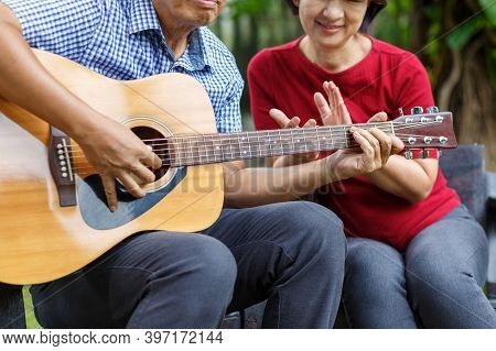 Middle Aged  Couple Playing Guitar While Relax Sitting On Bench In Backyard.