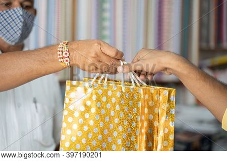 Closeup Of Shopkeeper In Medical Mask Handover Bag To Customer At Cloth Store - Concept Of Buying Lo