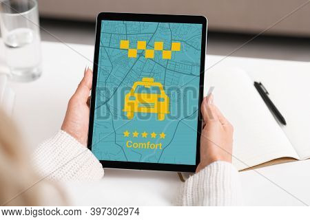 Businesswoman Holding Digital Tablet With Comfort Taxi App On Screen, Sitting At Desk In Office, Usi