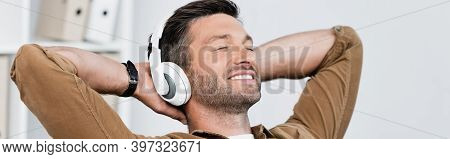 Businessman In Headphones, With Hands Behind Head And Listening To Music On Blurred Background, Bann