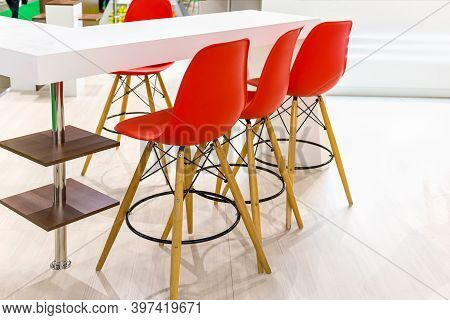 Three Red Bar Stools On Wooden Legs Stand Next To The Light Bar Counter