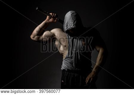 Dangerous Muscular Man In The Mask With Baseball Bat Ready For Fight. An Aggressive Hooded Man Is Ho