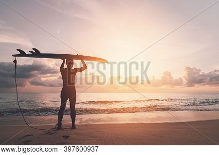 Man Hold Surfboard Standing At Tropical Sunset Beach Background. Summer Vacation And Sport Adventrue