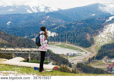 Happy Tourist Girl In Colored Jacket Standing On Observation Deck In Mountains Covered Snow