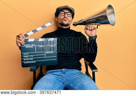 Handsome man with tattoos holding video film clapboard and louder looking at the camera blowing a kiss being lovely and sexy. love expression. 