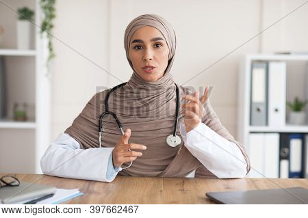 Woman In Hijab Doctor With Stethoscope Explaining Patient Diagnosis Or Treatment While Sitting At Wo