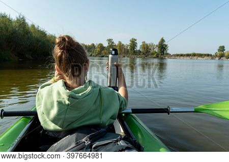 The Girl In The Boat Holds A Thermos For Tea. Rafting Down The River With A Thermos. The Girl Is Raf