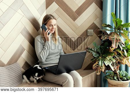 Adoult Woman 35s Working On Laptop And Talking On The Phone At Home, Cute Small Dog Besides. Work Fr