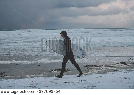 Arctic surfer going by beach after surfing