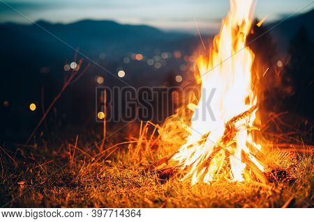 Bonfire In The Mountains Against The Background Of City Lights In The Bokeh.