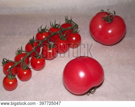 Two Large Tomatoes And Cherry Tomatoes On Branches Close Up On A Beige Background. High Quality Phot