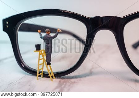 Optician Eyeglasses Being Cleaned By Tiny Figurine Symbolizing Clear Vision