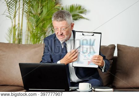 Experinced Middle-aged Businessman Pointing At Financial Chart When Talking To Colleague At Online C