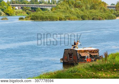 Man Playing Guitar While Sitting In A Chair On The Roof Of A Floating Raft Like A House. France, Blo