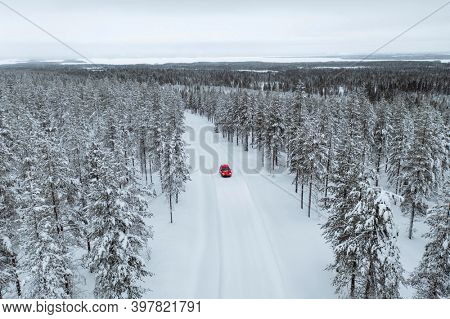 Drone view of a red car driving though a snowy forest in Lapland, Finland