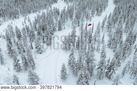 Drone view of a red car driving though a snowy forest in Lapland, Finland