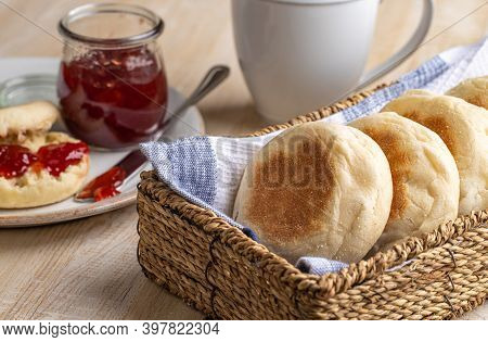 English Muffins In A Basket With A Muffin And Preserves In Background On A Wooden Table