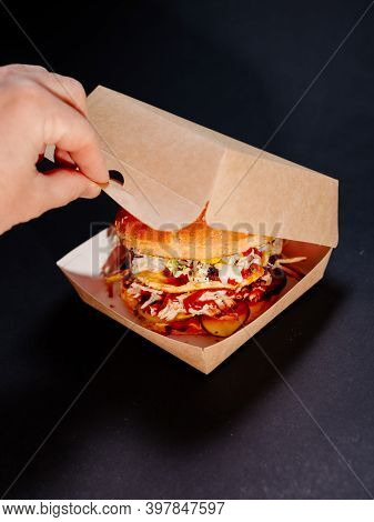 A Man's Hand Opens A Burger Box On A Dark Background. Burger With Whole Meat And An Omelet In A Pape