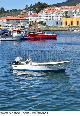Portosin, Spain. July 3, 2020. Small White Motor Boat Moored In A Harbor With Galician Fishing Vesse