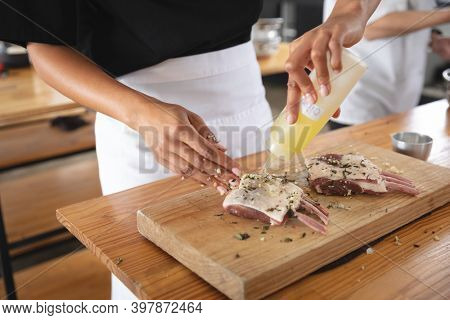 Divserse group of chefs in kitchen. trainee chefs standing at a table, preparing meat with seasonings.