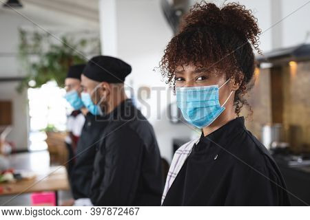 Divserse group wearing face masks in kitchen. portrait of trainee female chef looking at camera. hygiene in professional kitchen during coronavirus covid 19 pandemic.