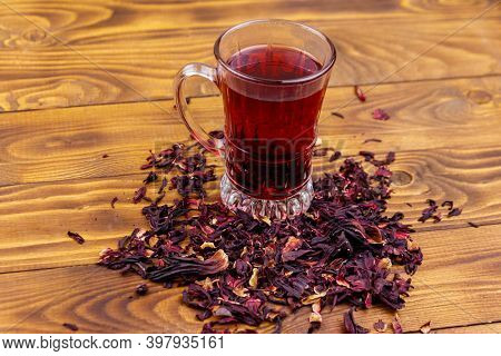 Glass Cup Of Red Hibiscus Tea (carcade, Roselle) On Wooden Table