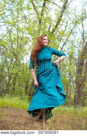 Bootless Woman Dance In Forest. Barefoot Girl In Elegant Dress Posing In Forest On Green Trees Backg