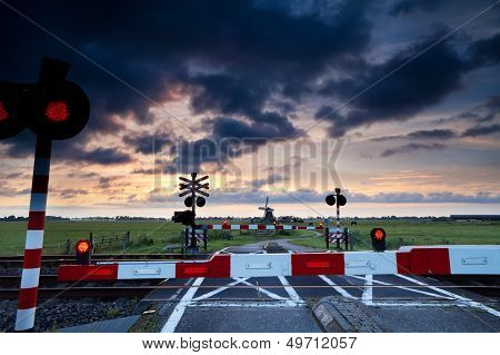 Closed Rail Crossing At Sunrise And Windmill