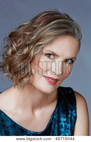 Mooie veertig jaar oude vrouw met fashion make-up, krullend kapsel op grijs blauw studio achtergrond.