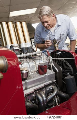 Senior man looking at car engine in automobile repair shop