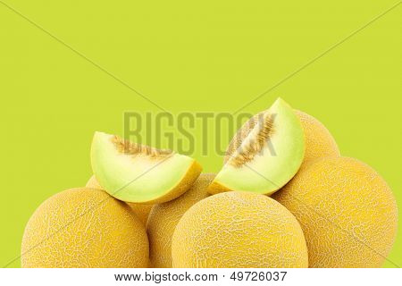 fresh galia melons and some cut pieces on a green background