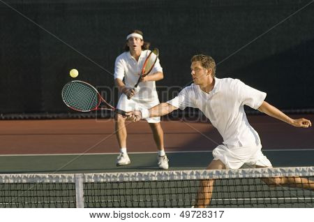Young male tennis player hitting ball with doubles partner standing in background