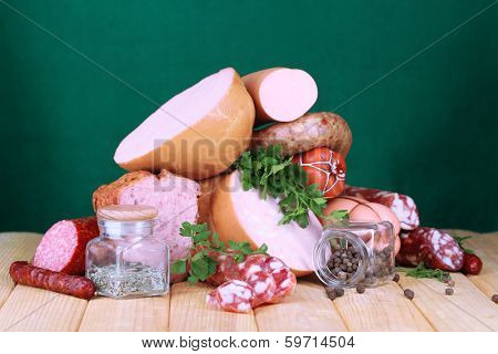 Lot of different sausages on wooden table on green background