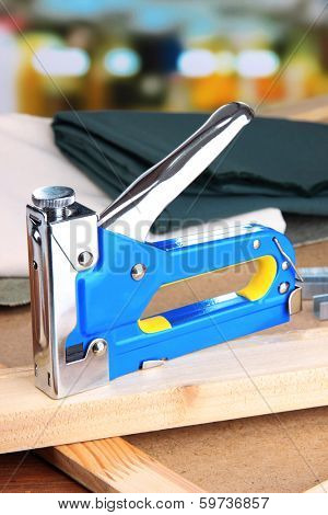 Construction stapler with fabric on cork board on bright background