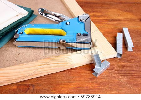 Construction stapler with fabrics and staples on cork board on wooden background