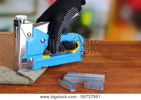 Fastening fabric and board using construction stapler on bright background
