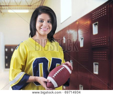 A beautiful teen girl happily holding a football in a locker room. 
