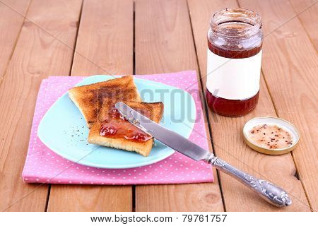 Toast bread spread with jam on plate and napkin with knife near jar on wooden table background