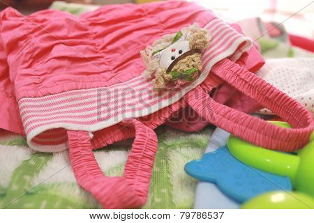 Little girl's pink dress lying on bed with toys and blanket
